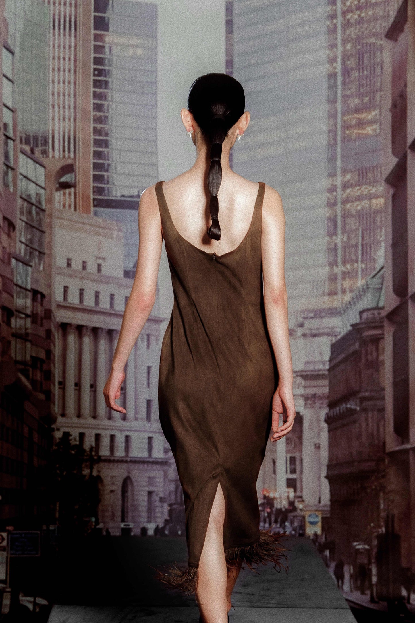 Woman in a brown dress walking away from the camera with a cityscape in the background