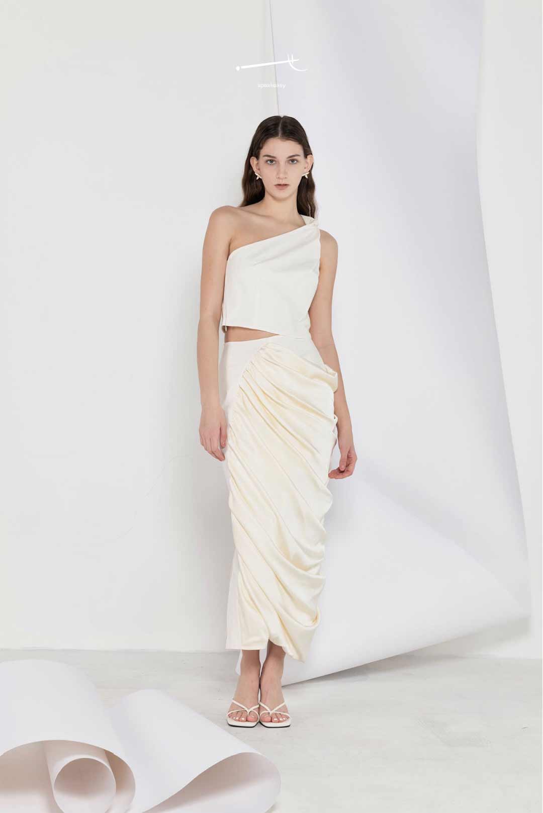 Model in one-shoulder cream top and
draped patchwork skirt