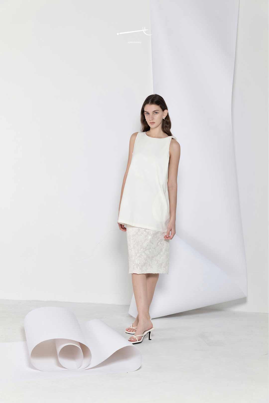 Woman wearing a white sleeveless top and skirt standing against a white background