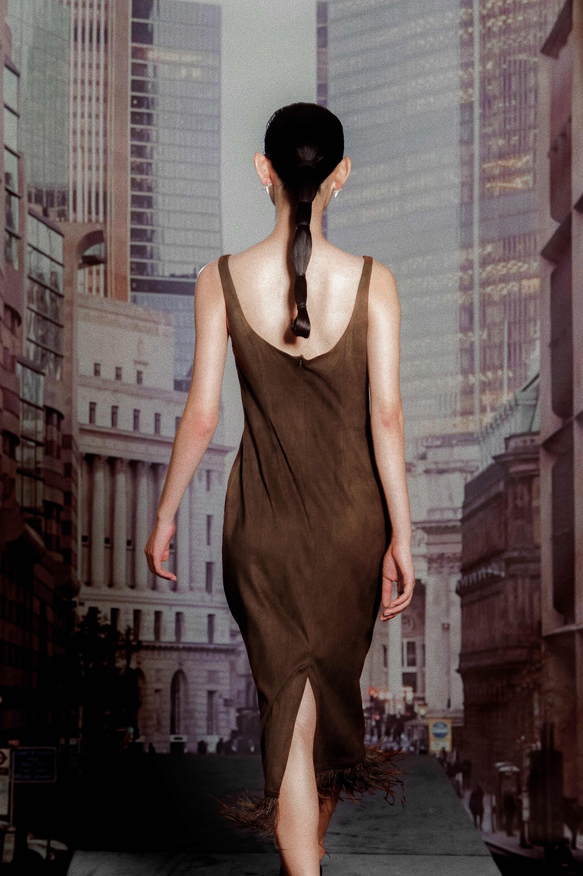 Woman in a brown dress walking away from the camera with a cityscape in the background