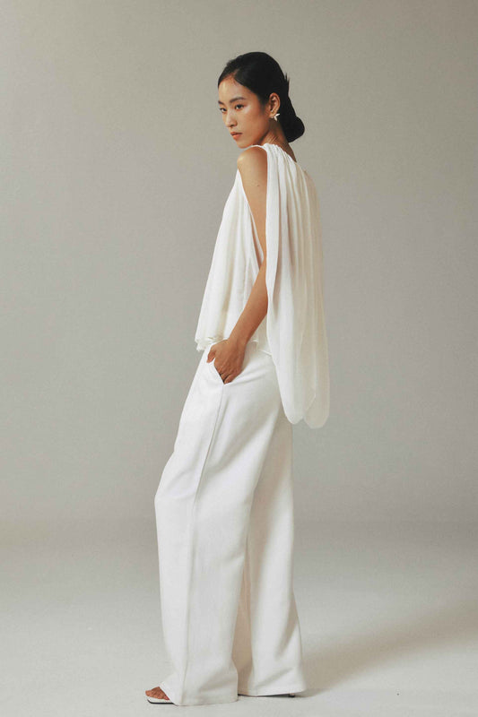 Woman wearing a white outfit with a draped top against a plain background