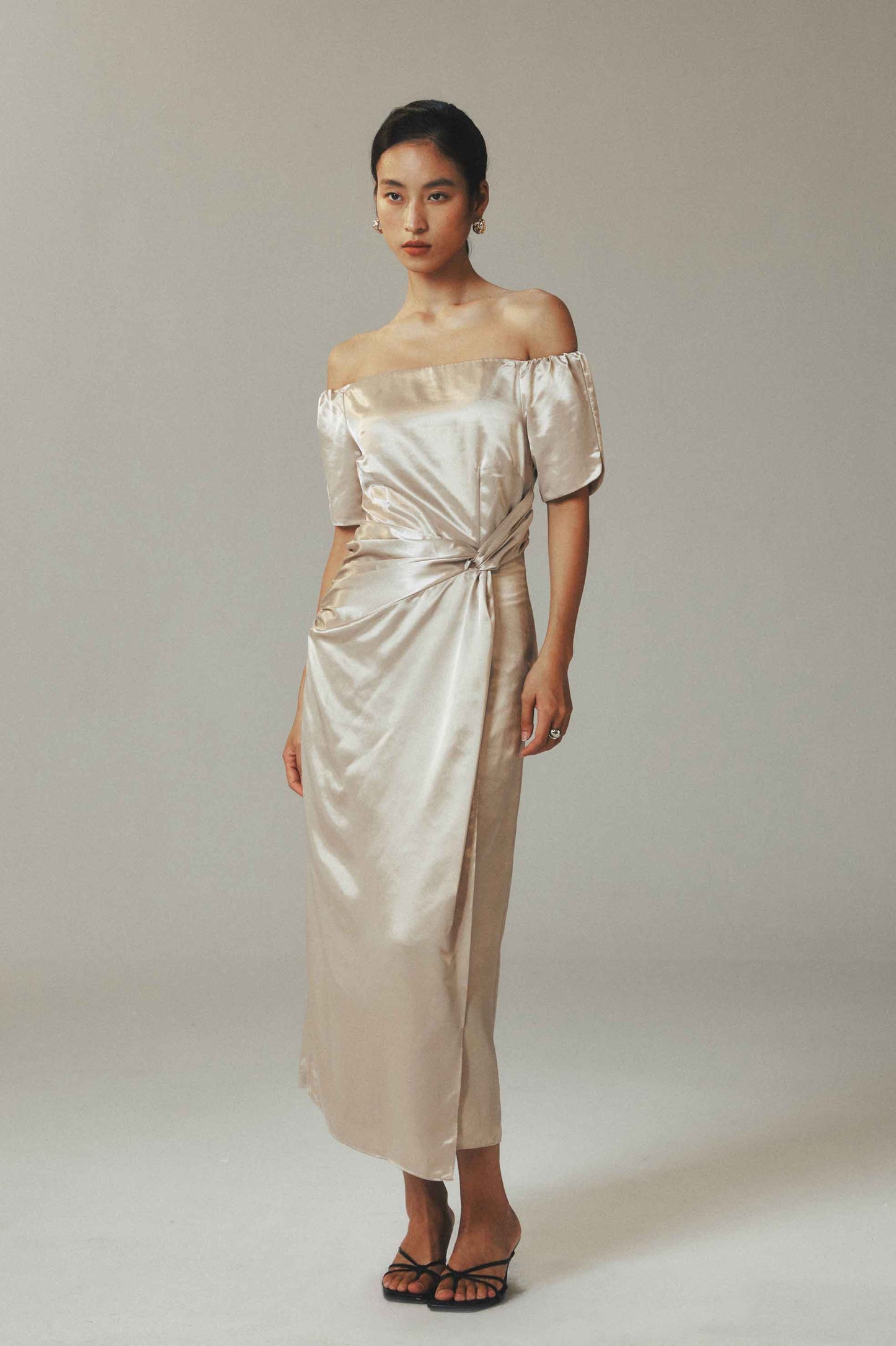 Model wearing off the shoulder maxi
dress in ice-silk fabric with button-pleated
detail