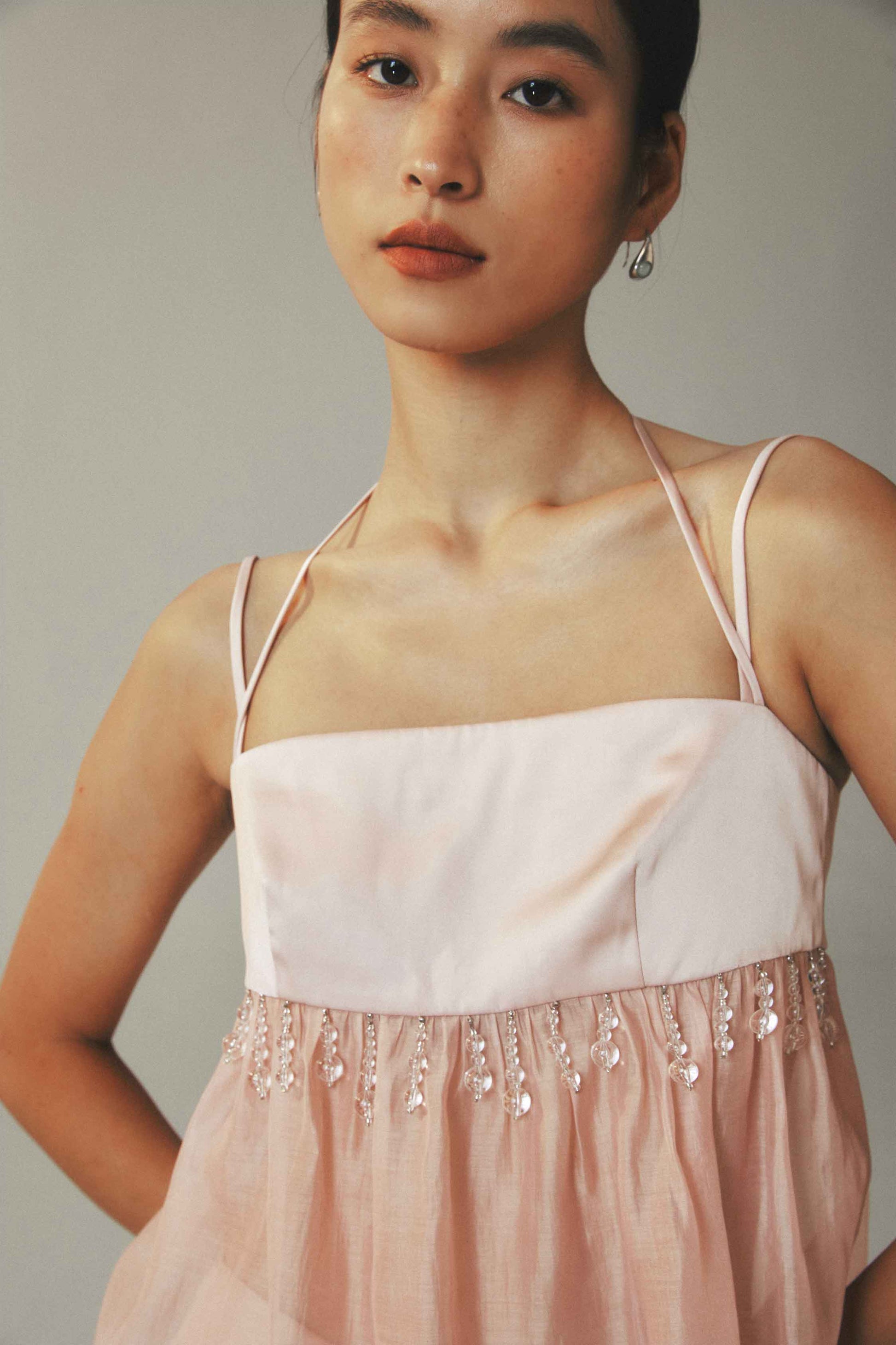 Woman wearing a light pink dress with thin straps and bead details on a plain background