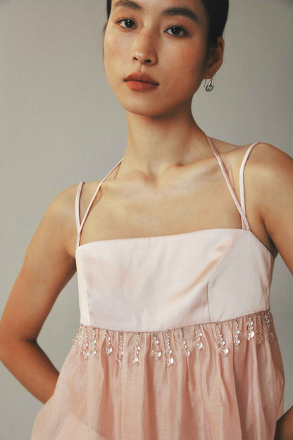 Woman wearing a light pink dress with thin straps and bead details on a plain background