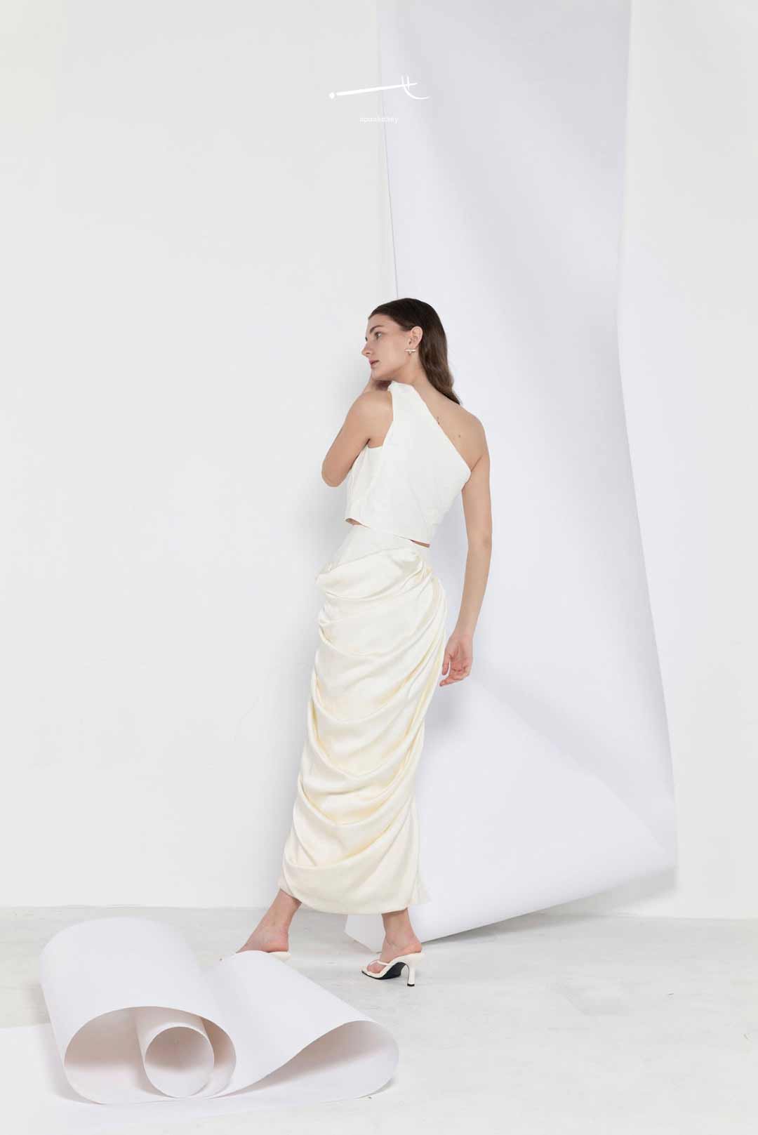 Model in one-shoulder cream top and
draped patchwork skirt